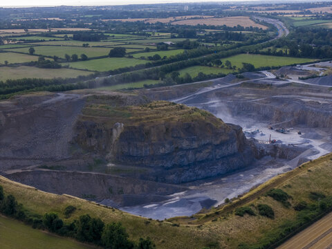 Aerial view of a large open-pit stone quarry with exposed rock faces, gravel piles, and heavy machinery in the rural landscape of Drogheda, County Louth, Ireland.