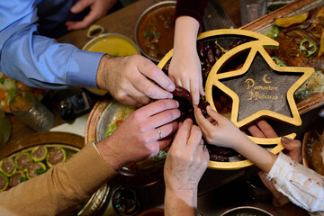Fototapeta premium Family Sharing Dates At Ramadan Iftar Dinner With Hands Reaching For Dates And Traditional Foods
