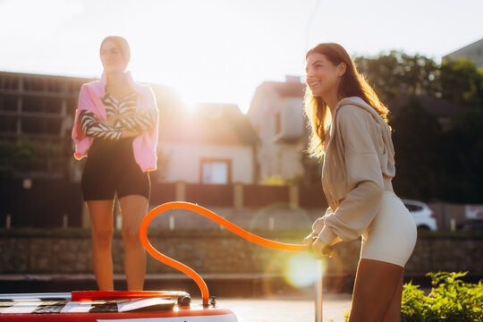 Young women friends inflating paddleboard before summer workout
