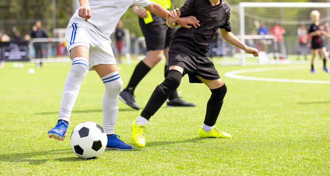 Junior Soccer Players in White and Black Kits Battling for Ball Control - Action Shot of Competitive Match on Turf Field