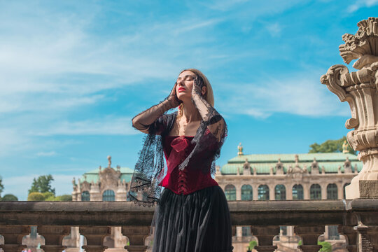 Beautiful woman in dark red velvet corset and black lace veil posing against historic Zwinger palace architecture in Dresden, gothic style and baroque aesthetics concept 