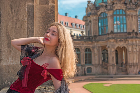Beautiful woman in dark red velvet corset and black lace veil posing against historic Zwinger palace architecture in Dresden, gothic style and baroque aesthetics concept 