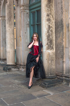 Beautiful woman in dark red velvet corset and black lace veil posing against historic Zwinger palace architecture in Dresden, gothic style and baroque aesthetics concept 