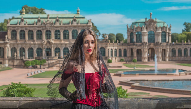 Beautiful woman in dark red velvet corset and black lace veil posing against historic Zwinger palace architecture in Dresden, gothic style and baroque aesthetics concept 