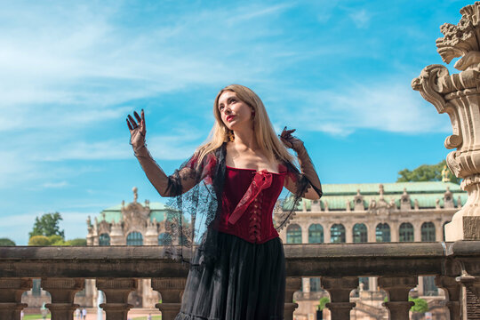 Beautiful woman in dark red velvet corset and black lace veil posing against historic Zwinger palace architecture in Dresden, gothic style and baroque aesthetics concept 