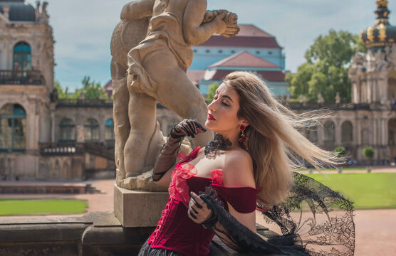 Beautiful woman in dark red velvet corset and black lace veil posing against historic Zwinger palace architecture in Dresden, gothic style and baroque aesthetics concept 