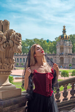 Beautiful woman in dark red velvet corset and black lace veil posing against historic Zwinger palace architecture in Dresden, gothic style and baroque aesthetics concept 