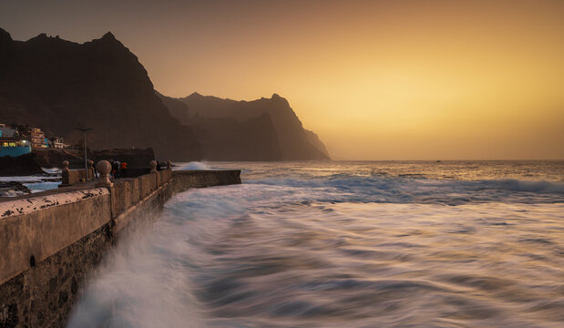 View of the rugged coastline of Santo Antao with waves crashing against the stone seawall at sunset in Ponta do Sol, Ribeira Grande, Cabo Verde.