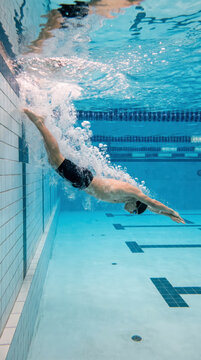 Skilled swimmer diving underwater off the wall in an indoor urban pool