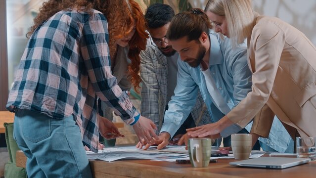 Casual informal business team designers architects emotional discussing blueprint building project plan in office five partners discuss talking job documents group architecture work process women men