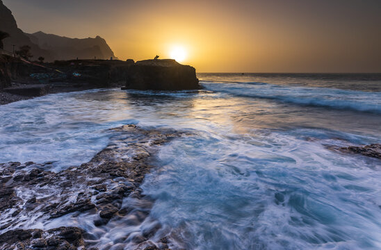 View of the sunset over the rugged volcanic coastline of Santo Antao with crashing waves and golden light in Ponta do Sol, Ribeira Grande, Cabo Verde.