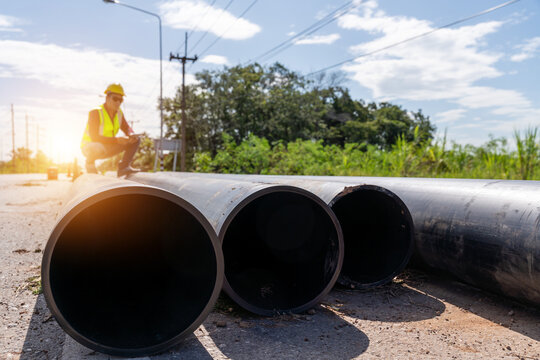 Large HDPE water supply pipes prepared for roadside installation with a worker inspecting the site, representing pipeline construction and water infrastructure development.