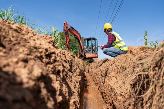 An Engineer inspecting trench excavation for water pipe installation with an excavator, representing pipeline construction, civil engineering and water infrastructure development.