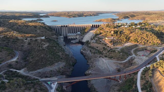 Aerial view of the concrete Alcantara Dam structure spanning the river with a bridge in the foreground and surrounding hills in Alcantara, Extremadura, Spain.