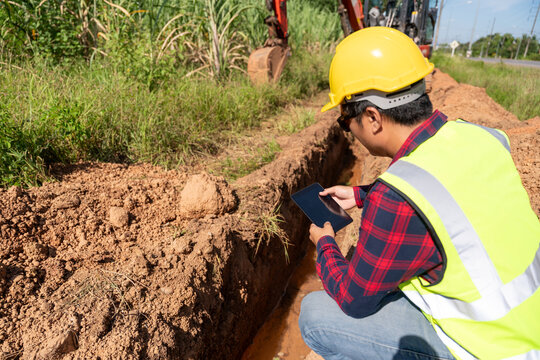 An Engineer using a tablet to inspect trench excavation prepared for water pipe installation, representing pipeline construction, civil engineering and water infrastructure.