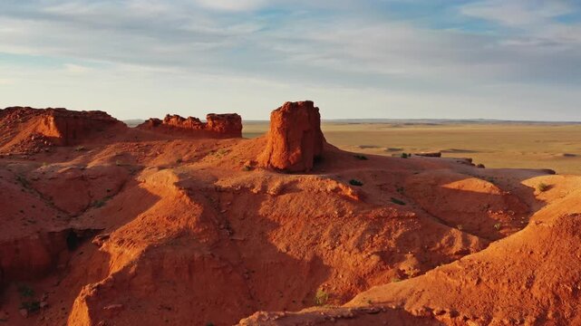 Aerial view of the iconic red sandstone formations of the Flaming Cliffs at golden hour in the vast desert landscape of Bulgan, Omnogovi, Mongolia.