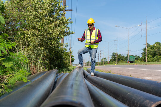 Asian Engineer inspecting large HDPE water supply pipes prepared for roadside installation, representing pipeline construction, quality control and water infrastructure development.