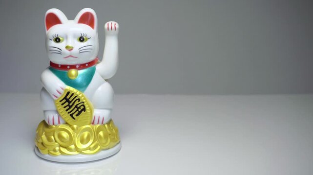Hand moving Chinese lucky cat Maneki Neko figurine across frame different directions
