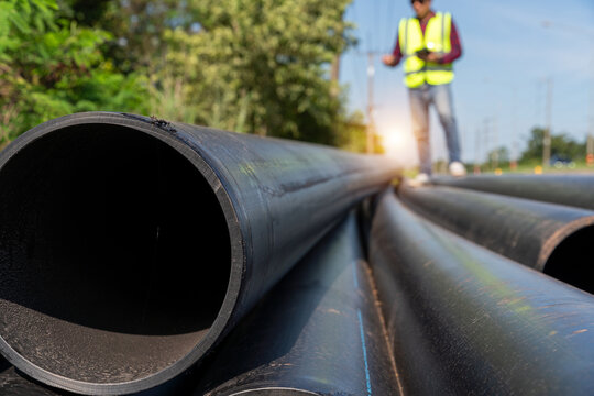 Large HDPE water supply pipes prepared for installation with engineer inspecting pipeline at roadside construction site, public utility and water infrastructure development.