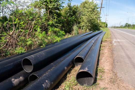 Large HDPE water supply pipes prepared for installation along roadside, pipeline construction materials for water distribution and public utility infrastructure development.