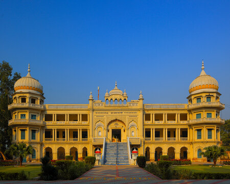 View of the historic Gurudwara Sacha Sauda with its yellow facade, symmetrical domes, and arched windows under a clear blue sky in Farooqabad, Punjab, Pakistan.