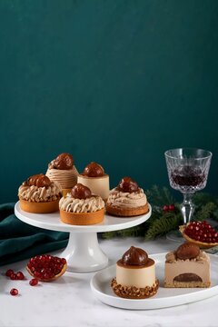 Candied chestnut pastries on a white cake stand. Festive Mont Blanc desserts with cream and chestnuts on a dark green background