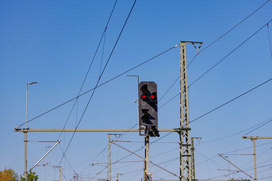 German railway red stop signal light against blue sky with overhead electric catenary power lines, train transport and safety concept