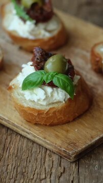 Vertical video. Bruschetta or crostini with cream cheese, sun-dried tomato, olive and fresh herbs. Tasty healthy snacks.