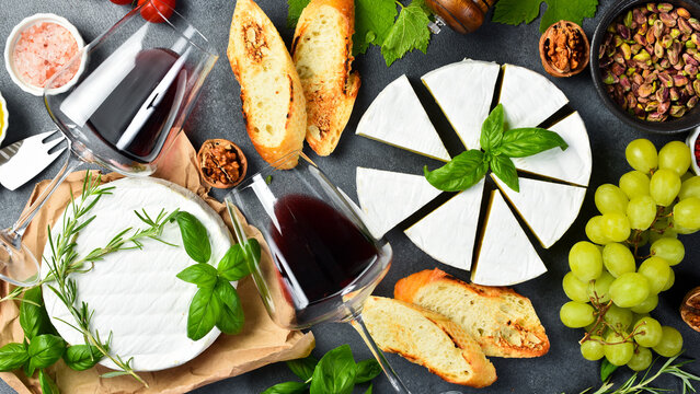 Cheese and wine background. Brie cheese, glasses of wine, nuts and grapes on a table with basil, olive oil and toasted bread. On a stone background. Top view.