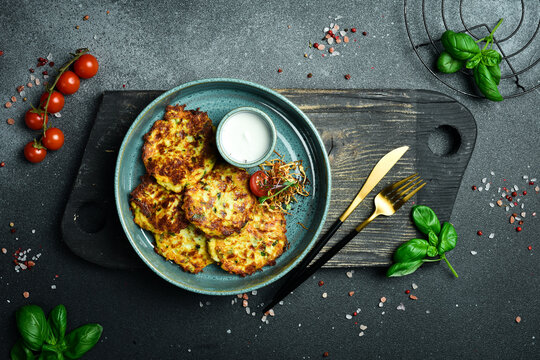 Fried potato pancakes with spinach and sour cream. Ukrainian cuisine. Close up. On a dark stone background.