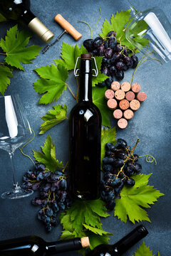 Red Bottles of wine, bunch of grapes, glasses, corkscrew and corks on dark textured table. Top view.