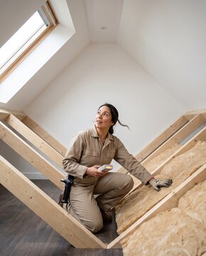 Energy consultant kneeling in an attic to inspect the roof insulation of a house