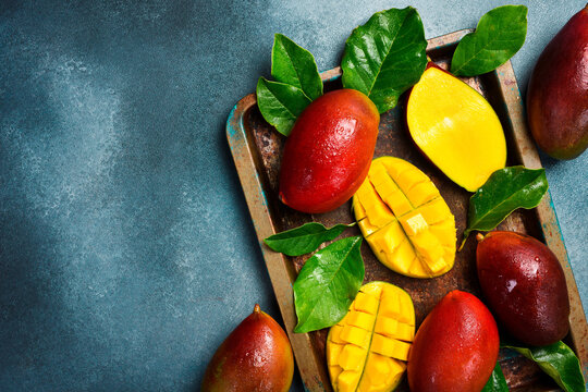 Ripe whole red mango fruits with leaves on a metal tray. Top view. Close-up.