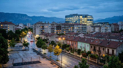 Fototapeta premium City street with residential buildings and modern office block at dusk. Urban neighborhood with illuminated windows and wet road during twilight
