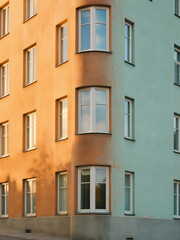 Fototapeta premium Vertical photo of a colorful residential building corner with curved windows. Orange and green painted apartment facade in sunlight