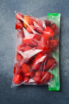 Frozen strawberries in a plastic bag. Stocks of frozen berries for the winter. On a gray concrete background.