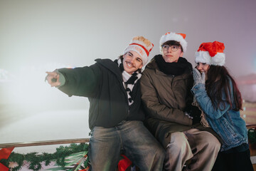 Fototapeta premium Three friends in winter coats and Santa hats sit together and smile at an outdoor ice rink. A festive group enjoys a chilly evening by the decorated skating rink.