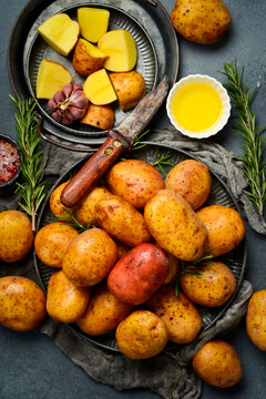Raw organic potatoes, rosemary, oil and spices. Cooking background. On a gray stone kitchen table.