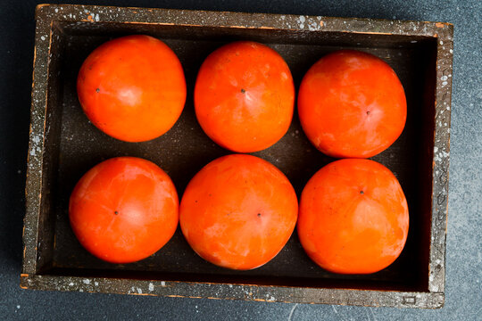 Wooden box with fresh persimmons. Autumn fruits. On a dark background.