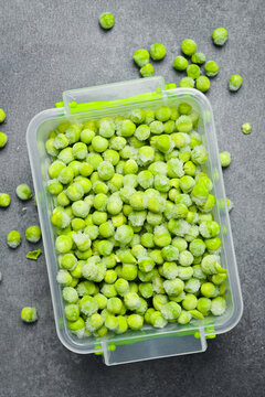 Frozen bunch of green peas in a plastic box. Frozen vegetables for the winter. On a gray stone background. Close-up.