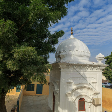 View of Gurudwara Patti Sahib with its white dome, surrounded by trees under a blue sky in Nankana Sahib, Punjab, Pakistan.