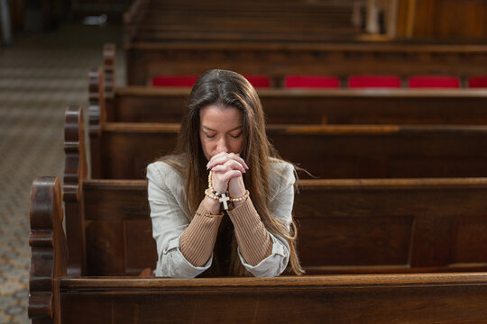 A woman is praying alone in a European Catholic church during Holy Mass. She shows devotion and faith through her prayer.