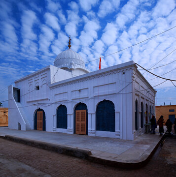 View of Gurudwara Patti Sahib with its white dome and arched doorways under a blue sky with scattered clouds in Nankana Sahib, Punjab, Pakistan.