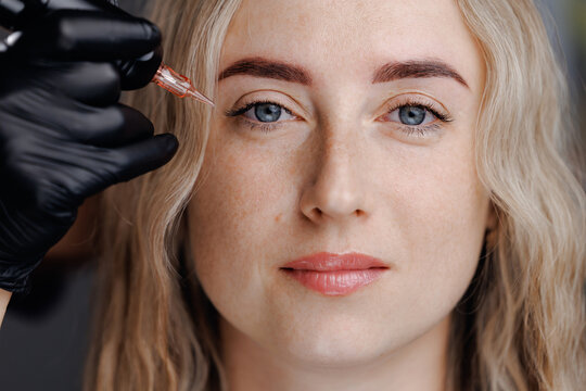 Young woman undergoing eyebrow microblading permanent procedure in studio
