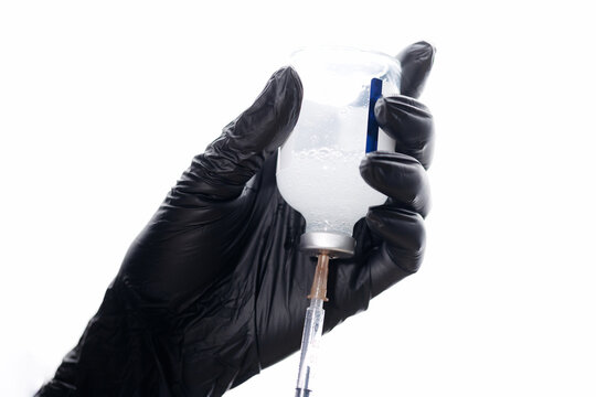 Gloved hand drawing liquid from vial with syringe in clinic
