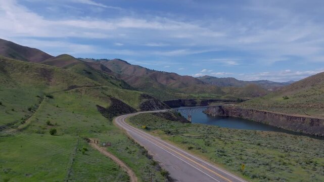 Aerial view of Lucky Peak Lake with rolling green hills, a winding road, and blue sky in Ada County, Idaho, United States.