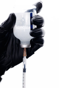 Gloved hands preparing injection by drawing vial into syringe
