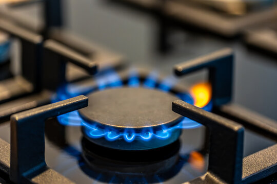 Gas stove burner with blue flame. Horizontal cooktop detail in kitchen.