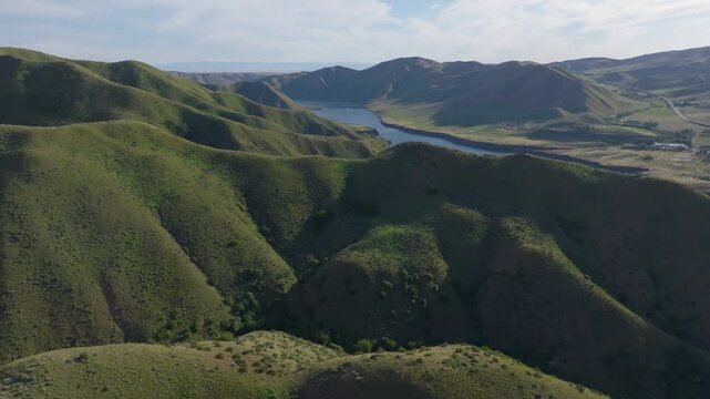 Aerial view of Lucky Peak Lake surrounded by rolling green hills and rugged terrain under a clear sky in Ada County, Idaho, United States.