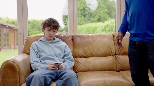 Teenager boy staring at phone and isn&rsquo;t paying any attention while man trying to call him, shouting at boy, concept of generation gap and communication problems within a family.